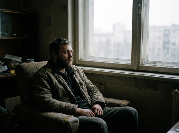 Мужчина в пустой комнате смотрит в окно, символизируя чувство опустошения и поиск смысла.